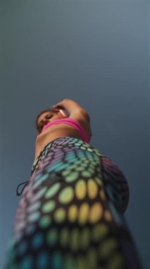 Parlak atletizm kıyafetleri içinde zarif bir sporcu kadın, sokak fitness rutinleriyle uğraşırken aşağıdan görülüyor. Yüksek kalite 4k görüntü