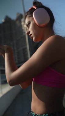 Renkli atletizm kıyafetleri içinde zarif bir sporcu kadın şehir sokaklarında aktif kalıyor ve yaz güneşinin tadını çıkarıyor. Yüksek kalite 4k görüntü