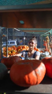 Pazar yerinde, enerjik genç bir bayan çiftçi satın alınabilir turuncu bir balkabağı gösteriyor. Yüksek kalite 4k görüntü