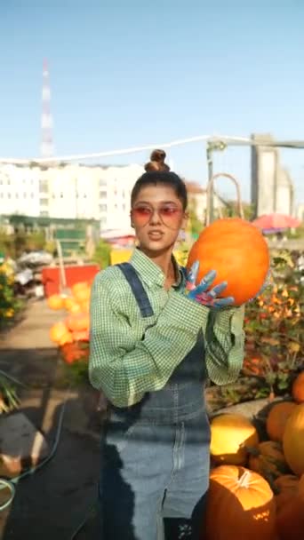 在市场摊位上 一位年轻的女农场主正在积极地展示这个巨大的橙色南瓜 作为她选择的一部分 高质量的4K镜头 — 图库视频影像