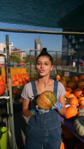 在市场上 一位年轻的女摊贩正拿着一个她正在卖的大橙色南瓜 高质量的4K镜头 — 图库视频影像