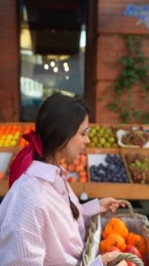 Güzel bir genç kadın Avrupa çiftçi pazarında sebzeleri bir sepete dikkatlice koyar. Yüksek kalite 4k görüntü