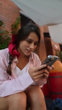 Pembe giyinmiş, akıllı telefonlu büyüleyici genç bir bayan çiftçi pazarına göz atıyor. Yüksek kalite 4k görüntü