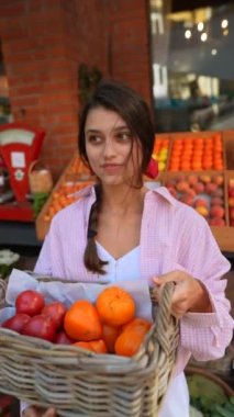 Avrupa çiftçi pazarındaki ışıl ışıl genç bir bayan, sepetteki sebzeleri organize ederken çevre dostu uygulamalarla gurur duyuyor. Yüksek kalite 4k görüntü