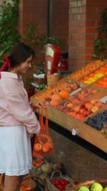 Avrupalı çiftçi pazarındaki büyüleyici genç bayan sürdürülebilirliği somutlaştırarak, çevre dostu bir çantayı meyvelerle dolduruyor. Yüksek kalite 4k görüntü