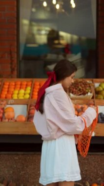 Avrupa 'daki mağazada, saçında pembe kurdele olan neşeli genç bir bayan meyve satın alıyor. Yüksek kalite 4k görüntü