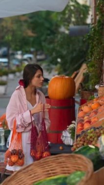 Avrupalı çiftçi pazarı, çevre dostu bir çantaya meyve doldururken çevreyle ilgilenen sevimli genç bir bayanla övünüyor. Yüksek kalite 4k görüntü