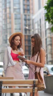 Şehir ortamında akıllı telefonları ve soğuk içecekleri olan iki çekici genç bayan. Yüksek kalite 4k görüntü
