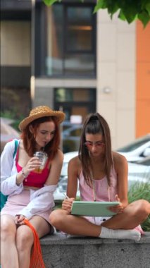 Şen, modaya uygun genç kadınlar şehir sokaklarında tabletler ve ferahlatıcı içeceklerle bir yer bulurlar. Yüksek kalite 4k görüntü