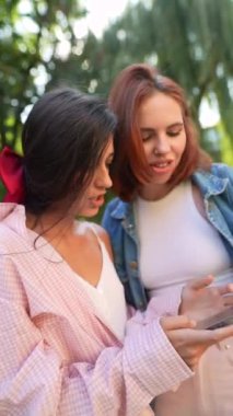 Açık havada akıllı telefonlarını tutarken sohbet eden bir çift çekici ve genç kız. Yüksek kalite 4k görüntü