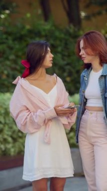 Elinde akıllı telefonlar olan iki güzel genç kadın şehrin sokaklarında konuşuyor. Yüksek kalite 4k görüntü