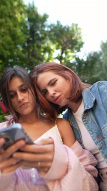 İki modaya uygun ve kendine güvenen kadın akıllı telefonlarını kullanırken şehir sokaklarında öylesine sohbet ediyorlar. Yüksek kalite 4k görüntü