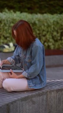 Sıcak bir yaz gününde dışarıda tablet üzerinde çalışan çekici, genç bir bayan. Yüksek kalite 4k görüntü