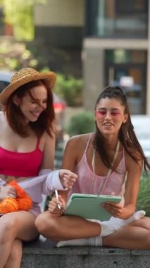 İki sevimli genç kız güneşli bir yaz gününde online işler için bir tablet kullanıyorlar. Yüksek kalite 4k görüntü