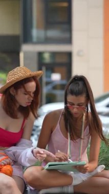 Şehirde açık havada tablet üzerinde çalışan iki çekici kadın görülüyor. Yüksek kalite 4k görüntü