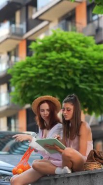Bir yaz günü sokakta elinde tablet ve biraz meyve olan iki güzel genç kadın oturuyor. Yüksek kalite 4k görüntü