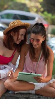 Bir yaz günü dışarıda, iki güzel genç bayan bir tablet üzerinde çalışıyorlar. Yüksek kalite 4k görüntü