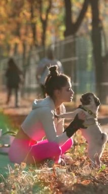 Sonbahar parkında, sportif bir kız mutlu bir şekilde pug dog 'u eğlendiriyor. Yüksek kalite 4k görüntü