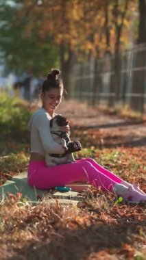Sonbahar manzarasının tadını çıkaran genç bir bayan parkta oturuyor ve köpeğiyle oynuyor. Yüksek kalite 4k görüntü