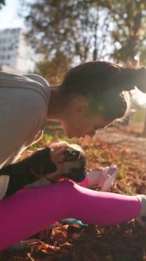 Sonbahar güneşinin ortasında, muhteşem bir kız pug köpeğiyle oynarken görülüyor. Yüksek kalite 4k görüntü