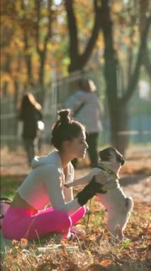 Güneşin parlamasıyla, genç bir kadın ve köpeği bir sonbahar gününde parkta neşeli bir kucaklaşmayı paylaşıyorlar. Yüksek kalite 4k görüntü