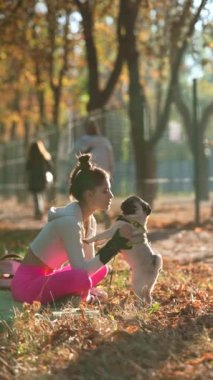 Pug seven genç bir bayan, spor giyim bölümünde, sonbahar parkında kürklü arkadaşıyla vakit geçiriyor. Yüksek kalite 4k görüntü