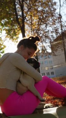 Sonbahar atmosferinin tadını çıkaran canlı bir kız, parkta köpeğiyle sıcak bir kucaklaşmayı paylaşıyor. Yüksek kalite 4k görüntü