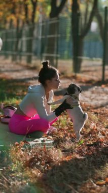 Sonbahar parkında, sportif genç bir kadın bir pug köpeğiyle oyun oynuyor. Yüksek kalite 4k görüntü
