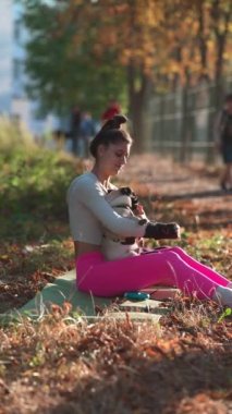Sarı yaprakların arasında oturan genç bir bayanın köpeğiyle şakalaştığı bir park sahnesi. Yüksek kalite 4k görüntü