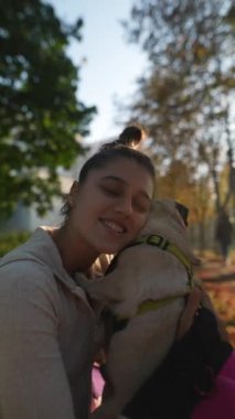 Parkta, güzel, genç bir kadın köpeğiyle birlikte sonbahar yapraklarıyla çevrili olarak otururken görülüyor. Yüksek kalite 4k görüntü