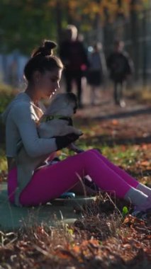 Sonbahar manzarasının tadını çıkaran spor giyimli bir kız, köpeğiyle parkta rahatça yürüyor. Yüksek kalite 4k görüntü