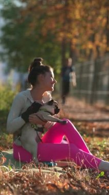 Sarı sonbahar yapraklarının arasında, genç bir kadın ve köpeği parkta neşeli bir an yaşıyorlar. Yüksek kalite 4k görüntü