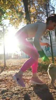 Sonbahar sabahı, sportif bir kız pug köpeğiyle yürürken görülüyor. Yüksek kalite 4k görüntü