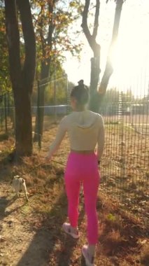 Köpeğiyle birlikte, sonbahar sezonu boyunca parkta yürüyüş yapan atletik giysili genç bir kadın var. Yüksek kalite 4k görüntü