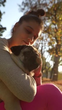 Parkta, güzel, genç bir kadın köpeğiyle birlikte sonbahar yapraklarıyla çevrili olarak otururken görülüyor. Yüksek kalite 4k görüntü