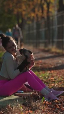 Parlak giyinmiş sportif bir kız, sonbahar parkında köpeğiyle yürüyüşe çıktı. Yüksek kalite 4k görüntü