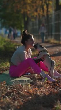 Parkta, canlı spor giyimli bir kız, sonbahar sezonunda köpeğiyle gezintiye çıkıyor. Yüksek kalite 4k görüntü