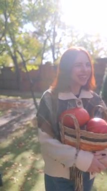 Gülümseyen, güzel genç bir kadın bir sonbahar gününde sepetinde bal kabakları taşıyor. Yüksek kalite 4k görüntü