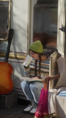 Sonbahar bahçesinde, elinde kitap ve sıcak bir içecek olan genç ve güzel bir kadın. Yüksek kalite 4k görüntü