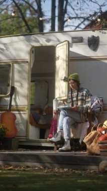 Sonbahar yapraklarının ortasında, hippi bir kız sıcak bir içeceğin tadını çıkarırken çalışmalarını tabletle sergiliyor. Yüksek kalite 4k görüntü