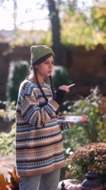 Hipster tarzını benimseyen şık ve ışıl ışıl genç bir bayan, sonbaharda güneşli bir günde tablet üzerinde çalışırken görülüyor. Yüksek kalite 4k görüntü