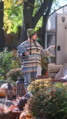 Sonbahar bahçesinde, sevimli genç bir hippi kadın sevimli bir karavanın yanında tablet üzerinde çalışıyor. Yüksek kalite 4k görüntü