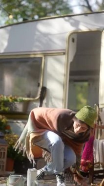 Hoş sonbahar havasında, renkli ve hippi dokunuşlu genç bir kadın römorkun yanında vakit geçirmekten zevk alıyor. Yüksek kalite 4k görüntü