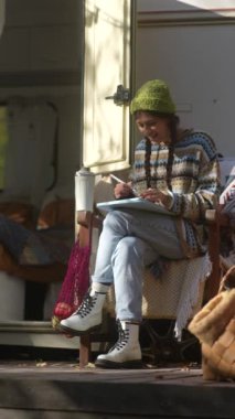 Hipster yaşam tarzını benimseyen şık ve genç bir kadın bahçede sıcak bir içki içerken tabletinde çalışıyor. Yüksek kalite 4k görüntü