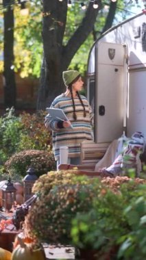 Hipster tarzını benimseyen şık ve güzel genç bir bayan bahçede büyüleyici bir karavanın yanında tabletini kullanırken görülüyor. Yüksek kalite 4k görüntü