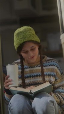 Hipster titreşimleriyle, güzel bir kız sonbahar bahçesinde bir kitap ve sıcak bir içeceğin tadını çıkarıyor. Yüksek kalite 4k görüntü