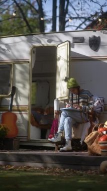 Bir hippinin çekiciliğiyle, genç ve güzel bir bayan, sonbahar bahçesinde tablet işine dalmış, yanında sıcak bir içecek ile. Yüksek kalite 4k görüntü