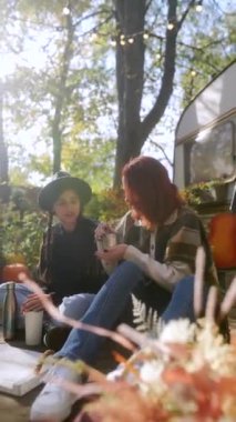 Hippi ruhlarını yayarak, iki genç kadın, altın sonbahar yaprakları arasında sıcak içeceklerinin tadını çıkarıyorlar. Yüksek kalite 4k görüntü