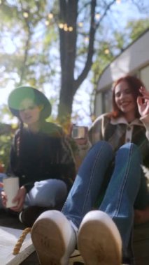 Moda ve hevesli iki kadın, tamamen hippi yaşam tarzına dalmış, sohbet ediyor ve karavanın yanındaki güzel sonbahar bahçesinde çaylarının tadını çıkarıyorlar. Yüksek kalite 4k görüntü