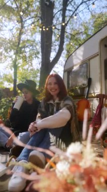 Gerçek hippi tarzında neşeli ve hayat dolu kızlar, karavanın yanındaki güzel sonbahar bahçesinde çay ve sohbetten zevk alırlar. Yüksek kalite 4k görüntü